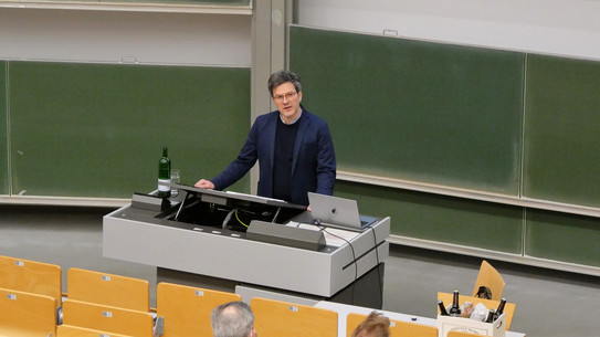 Das Foto zeigt Prof. Dr. Bernd Sommer bei seiner Antrittsvorlesung. Er steht unten am Rednerpult und schaut ins Auditorium.