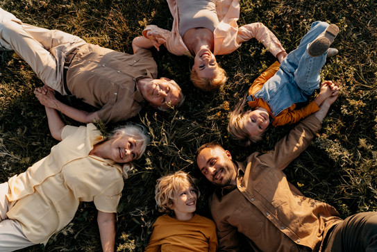 Eine Menschengruppe verschiedenen Alters liegt im Kreis lachend im Gras.
