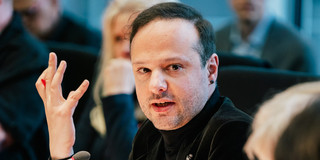 Francesco Cavallo sits at the conference table and gestures with his right hand.