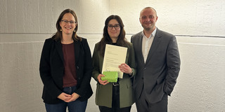 Imren Icel zeigt auf dem Foto ihre Urkunde für den Jahrgangsbestenpreis. Links neben ihr steht Prof. Dr. Dorothee Gronostay. Rechts von ihr steht Lukas Conrad Brandt.