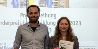 Julia Herbst und Dr. Schmalor nebeneinander auf der Preisverleihung, beide lächeln, Frau Herbst hält ihre Urkunde vor sich