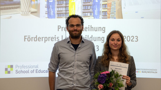 Julia Herbst und Dr. Schmalor nebeneinander auf der Preisverleihung, beide lächeln, Frau Herbst hält ihre Urkunde vor sich