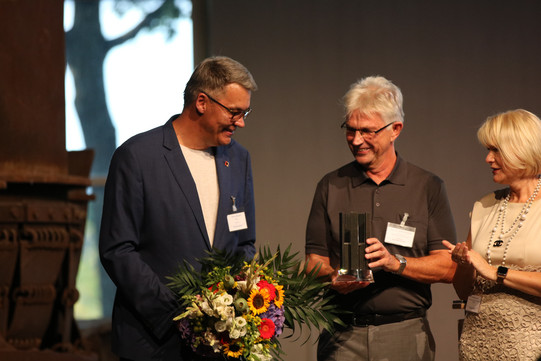 Herr Westphal und Frau Horster überreichen den Preis und einen Blumenstrauß an Herrn Howaldt.