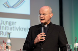Bischof Franz-Josef Overbeck bei der Podiumsdiskussion der Akademie „Die Wolfsburg“ mit Mikrofon in der Hand