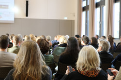Foto: Zuhörende sitzen in einem Seminarraum bei einer Präsentation.