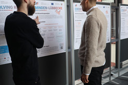 Zwei Personen stehen vor einem Plakat an einer Metaplantafel. Eine Person deutet auf das Plakat.