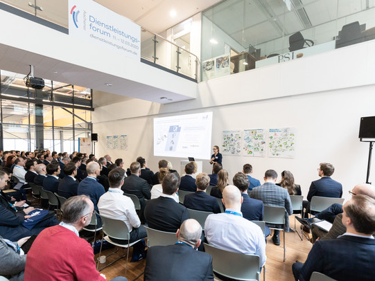 Foto einer Rede auf dem Aachener Dienstleistungsforum. Zu sehen ist die die Zuhörerschaft von hinten und die Bühne.