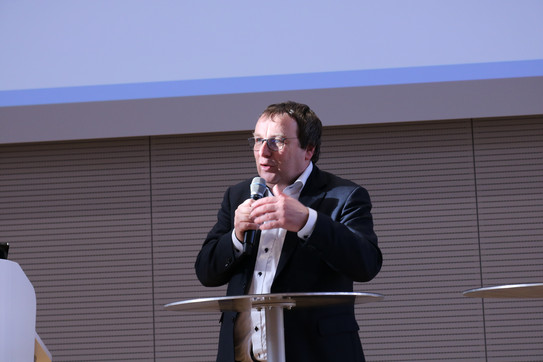 Minister Oliver Krischer Foto: Person spricht bei einer Veranstaltung und hält ein Mikrofon an einem Stehtisch.