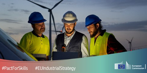 3 technicians stand in front of wind turbines and look at a computer.