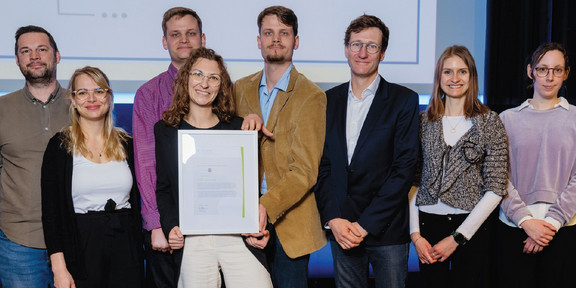 Group photo of eight people. Two people are holding a framed certificate.