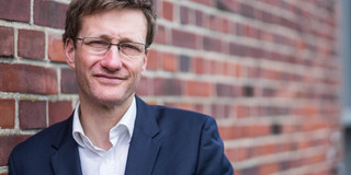 Portraitfoto von Dr. Bastian Pelka an einer rötlichen Ziegelwand
