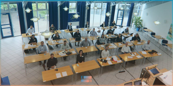 Foto: Personen sitzen an Tischen in einem hellen Seminarraum und nehmen an einer Veranstaltung teil.