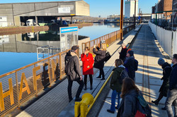 Foto: Gruppe von Personen steht an einem Hafenbecken und besichtigt das Gelände bei sonnigem Wetter.