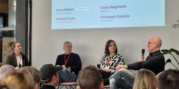 Zukunftsfabrik 2026 Ein großes Publikum aus Teilnehmenden der Zukunftsfabrik hört dem Panel zu, bestehend aus PD Dr. Christoph Kaletka von der SFS, Viola Stegmann (SEND e.V.) und Norbert Kunz (Social Impact gGmbH). Es moderiert Kiara Sobina (Social Impact gGmbH).