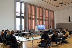 Foto: Personen sitzen in einem Konferenzraum und verfolgen eine Präsentation mit Bildschirm.