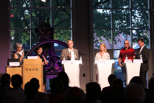 Die fünf Teilnehmenden und der Moderator, wie sie bei der Podiumsdiskussionen an Stehtischen stehen.