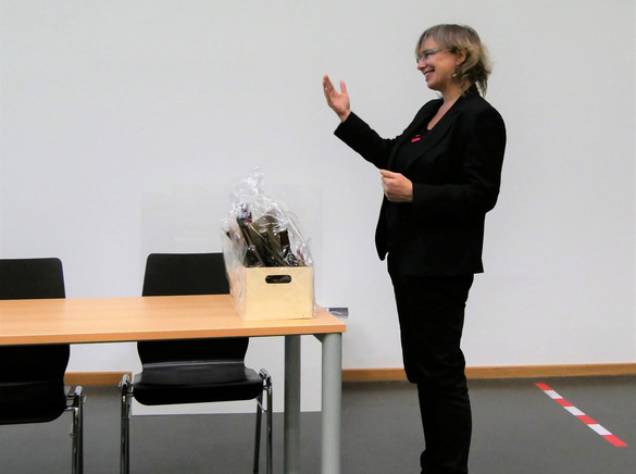  The photo shows Prof. Nicole Burzan, Dean of the Department of Social Sciences. She is standing at a table in the front of the lecture hall during Prof. Mona Motakef's inaugural lecture. In front of her is a small gift basket.