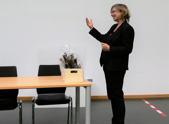 Nicole Burzan The photo shows Prof. Nicole Burzan, Dean of the Department of Social Sciences. She is standing at a table in the front of the lecture hall during Prof. Mona Motakef's inaugural lecture. In front of her is a small gift basket.