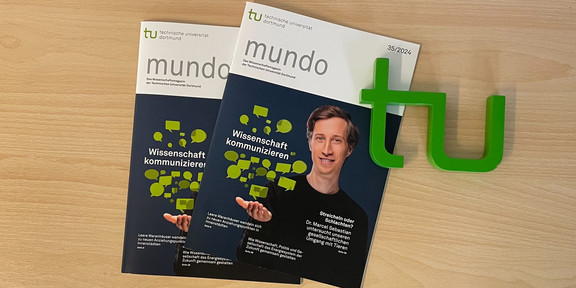 The photo shows two copies of mundo magazine and a TU logo lying on a table. Dr. Marcel Sebastian is pictured on the cover.