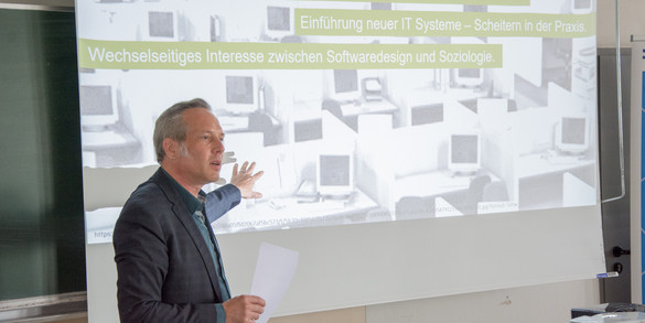 On the left of the photo is Prof. Cornelius Schubert, who is giving a lecture. In the background is a screen with a presentation to which Prof. Dr. Schubert is pointing.