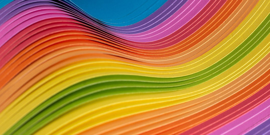Das abstrakte Bild besteht aus dünnen, übereinandergeschichteten Stoffen. Sie bilden eine Welle mit einem bunten Farbverlauf von blau am oberen linken und unteren rechten Rand über rosa, rot, orange, gelb und grün in der Bildmitte.