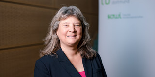 Nicole Stadtfeld Das Foto zeigt ein Porträt von Nicole Stadtfeld. Hinter ihr steth ein Rollup auf dem die Logos der Technischen Universität Dortmund und der Fakultät Sozialwissenschaften zu lesen sind.