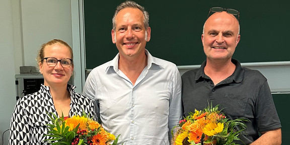 Auf dem Foto ist das neu gewählte Dekanat der Fakultät Sozialwissenschaften zu sehen. Links steht die wiedergewählte Prodekanin Forschung, Prof. Dr. Martina Brandt, mit einem Blumenstrauß in der Hand. In der Mitte steht der neugewählte Dekan, Prof. Dr. Cornelius Schubert. Rechts neben ihm steht der wiedergewählte Studiendekan, Dr. Arne Niederbacher, der ebenfalls einen Blumenstrauß in der Hand hält.