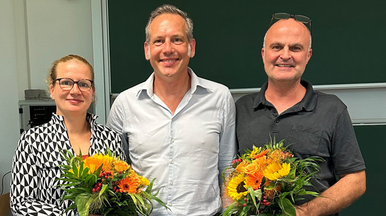 Auf dem Foto ist das neu gewählte Dekanat der Fakultät Sozialwissenschaften zu sehen. Links steht die wiedergewählte Prodekanin Forschung, Prof. Dr. Martina Brandt, mit einem Blumenstrauß in der Hand. In der Mitte steht der neugewählte Dekan, Prof. Dr. Cornelius Schubert. Rechts neben ihm steht der wiedergewählte Studiendekan, Dr. Arne Niederbacher, der ebenfalls einen Blumenstrauß in der Hand hält.