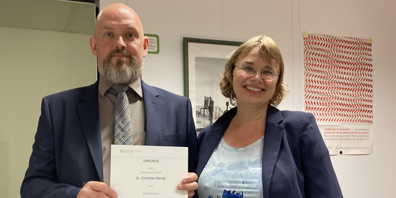 Auf dem Foto hält Dr. Christian Deindl die Ernennungsurkunde zum außerplanmäßigen Professor in den Händen, die er von der Dekanin Prof. Dr. Nicole Burzan erhalten hat. Sie steht neben ihm.