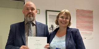 Auf dem Foto hält Dr. Christian Deindl die Ernennungsurkunde zum außerplanmäßigen Professor in den Händen, die er von der Dekanin Prof. Dr. Nicole Burzan erhalten hat. Sie steht neben ihm.