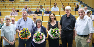 A group of six people, including the three new Vice-Presidents, are standing in the front row of a lecture theatre, holding colourful bouquets of flowers. They are smiling at the camera.