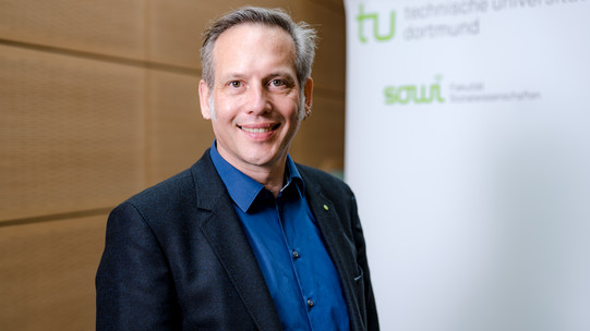 Prof. Dr. Cornelius Schubert The photo shows the portrait of Prof. Cornelius Schubert. Behind him is a rollup on which the logos of the TU Dortmund University and the Department of Social Sciences can be read.