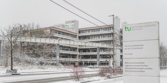 Schild mit Aufschrift Herzlich willkommen an der TU Dortmund, im Hintergrund das verschneite EF50-Gebäude.