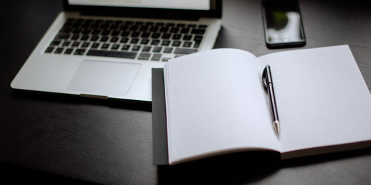 Turned on laptop, smartphone and notebook with pen lying on a table.