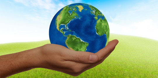 One hand holds a globe against the background of a green meadow with a blue sky.