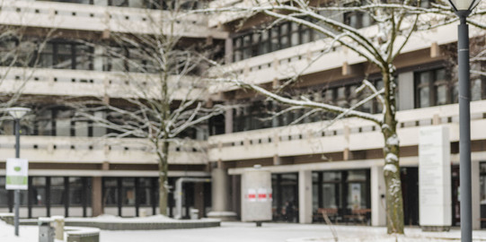 Vor dem Gebäude EF 50 steht eine Bank auf der Schnee liegt.