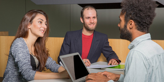 Studierende in Gesprächssituation Drei Studierende sitzen sich gegenüber und unterhalten sich.