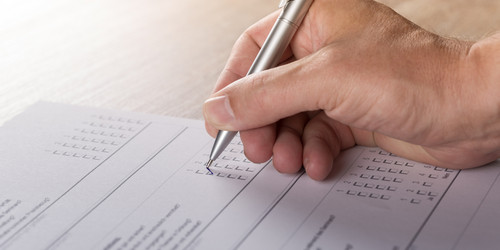 A hand holding a pen fills out a survey questionnaire.