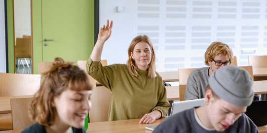 Studierende Handmeldung Studierende im Seminarraum sitzen an den Tischen. Eine Person meldet sich.